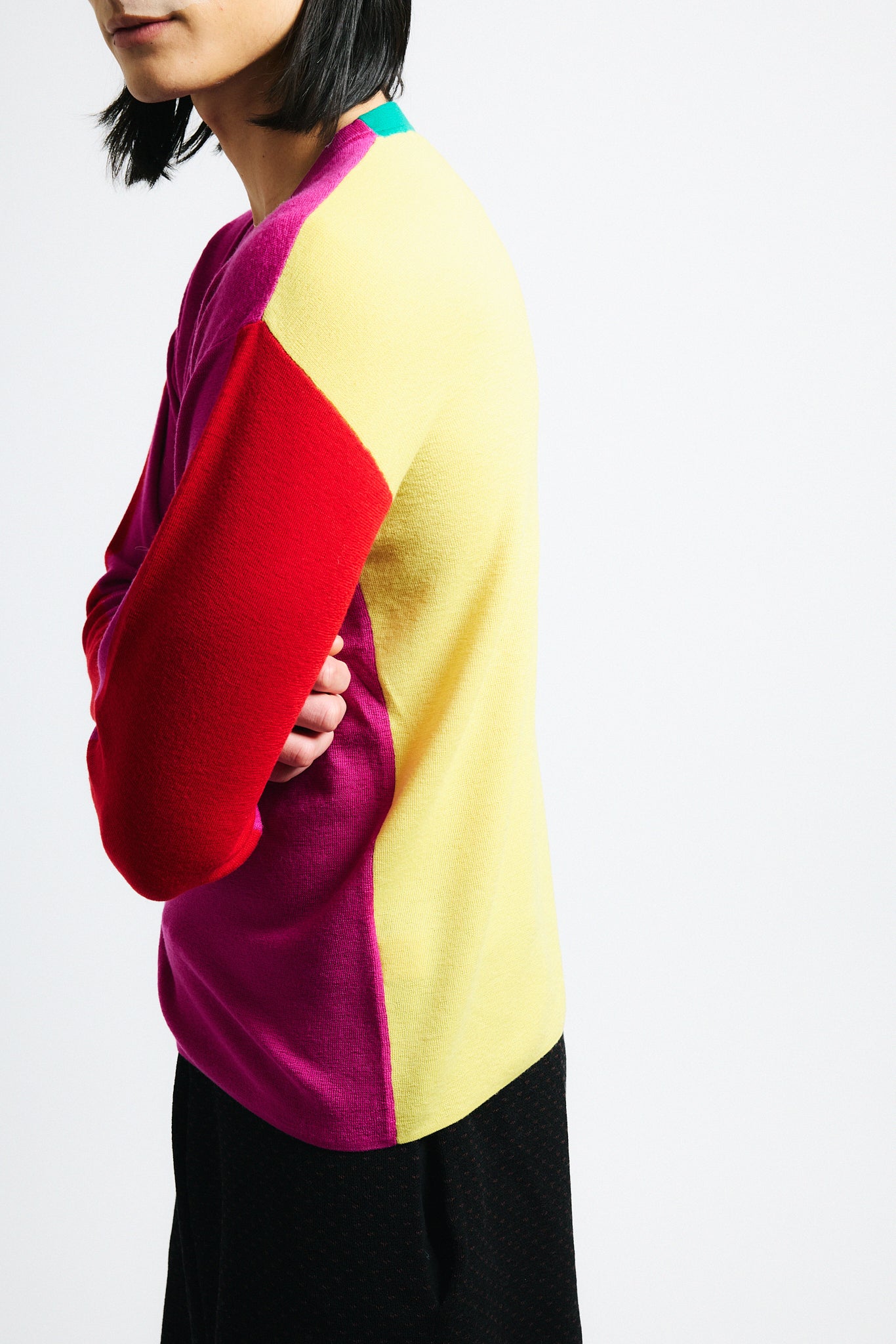 Link to "Julienne" sweater. Image is of a male model wearing magenta, red and yellow color-block sweater and black shorts. Front is pink with red sleeves and yellow back.