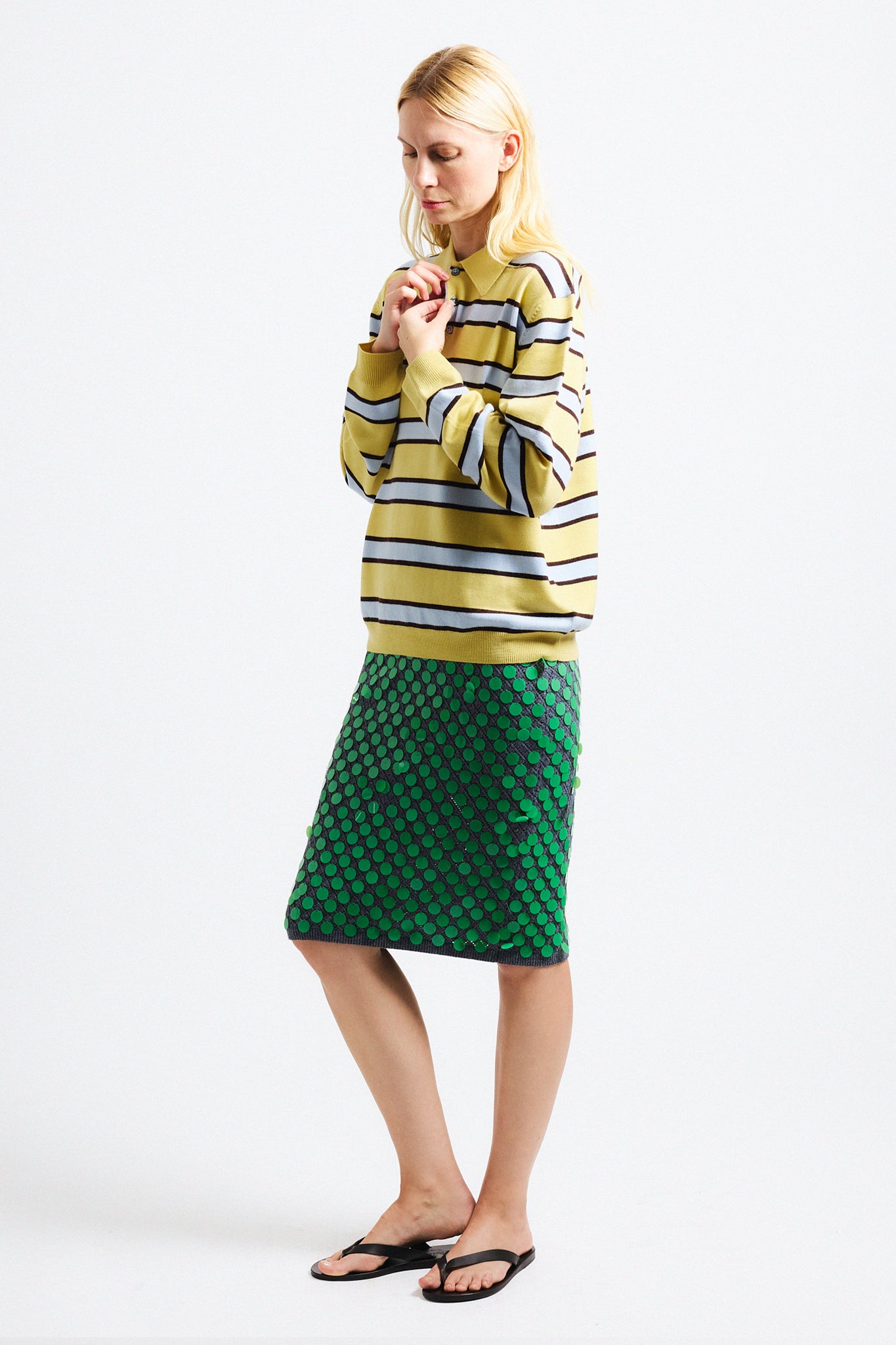 Link to "Ryan" sweater. Image is of a female model wearing yellow and grey striped polo with green sequin midi skirt.