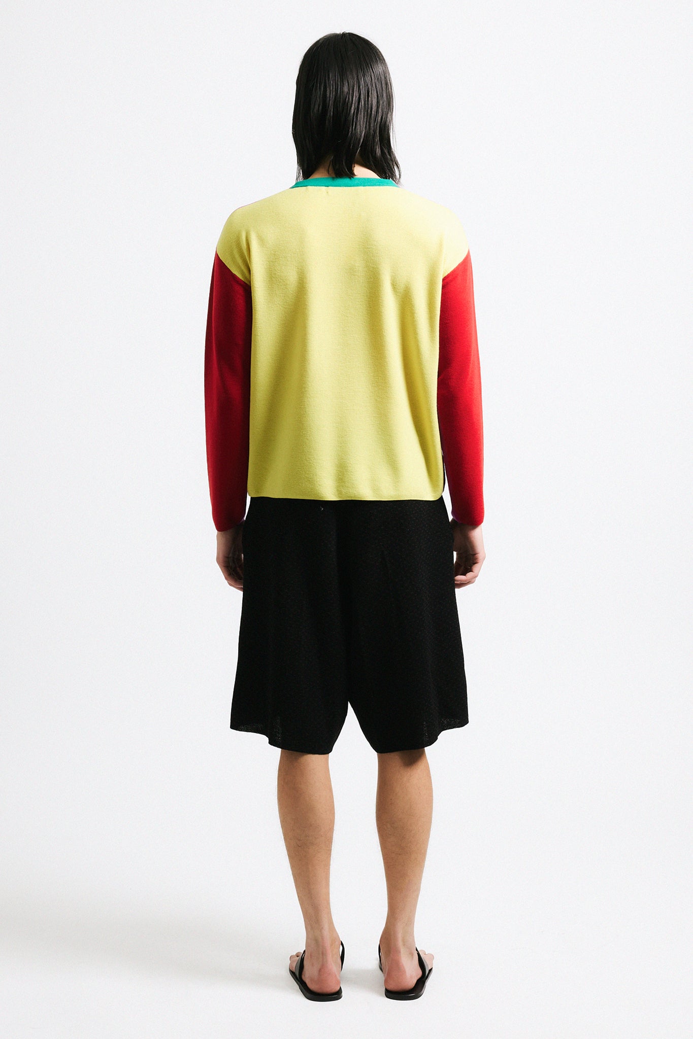 Link to "Julienne" sweater. Image is of a male model wearing magenta, red and yellow color-block sweater and black shorts. Front is pink with red sleeves and yellow back.