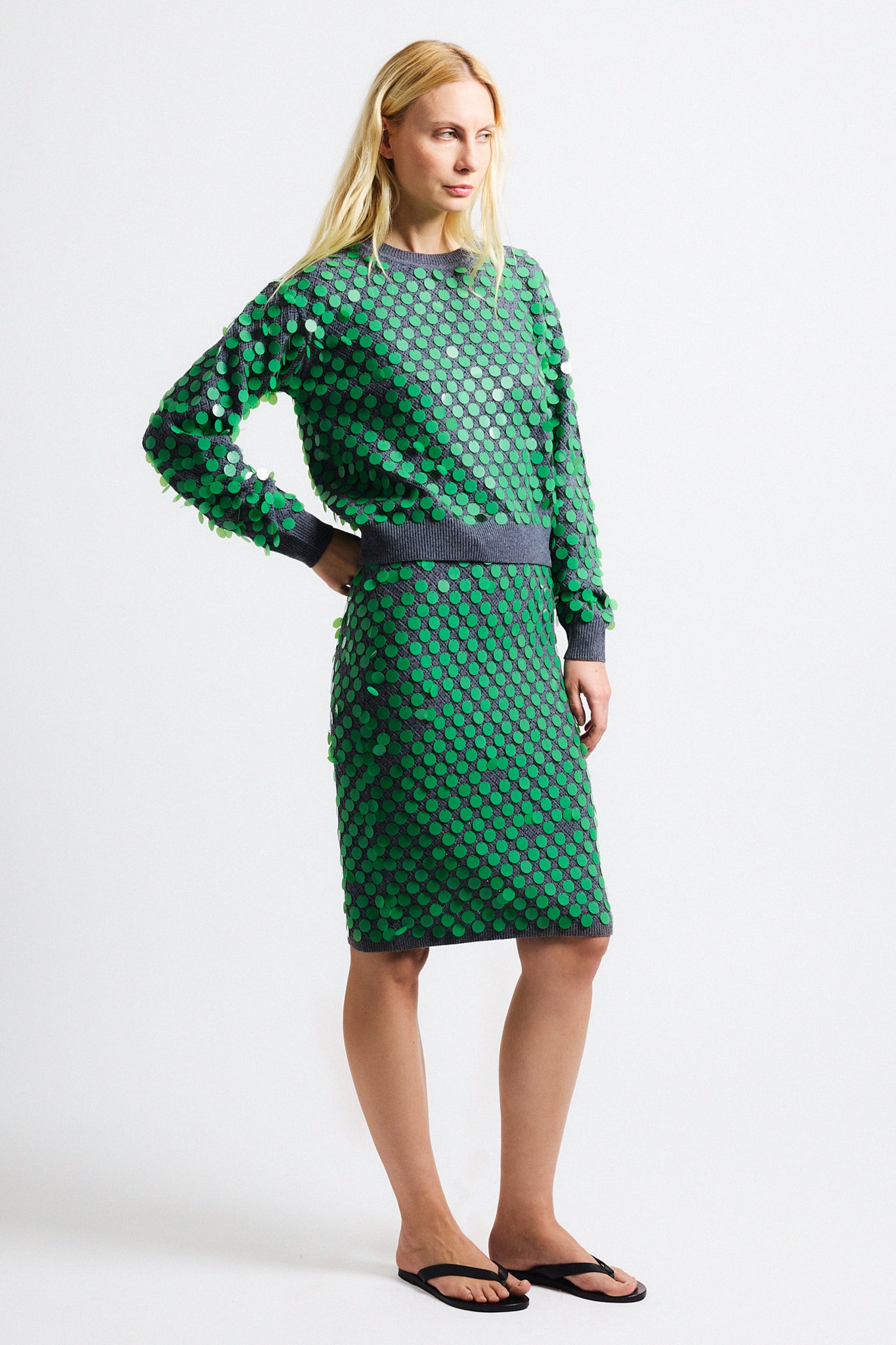 Link to "Ilaria" sweater. Image is of a female model wearing grey texture cropped crewneck sweater with green paillettes and matching pencil skirt.